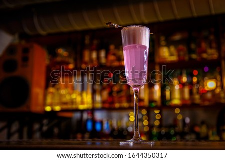A purple Sauer cocktail in a tall glass with foam stands on the bar