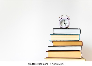 Purple small alarm clock on stack of books on white background wall with copy space. Concept of time to study, read books. Concept of preparing for exams