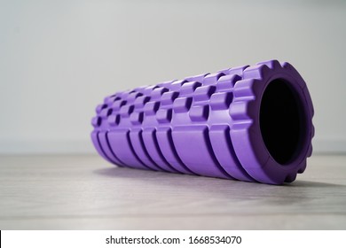 Purple textured foam roller for body massage on the light white wooden floor in front of the wall at home