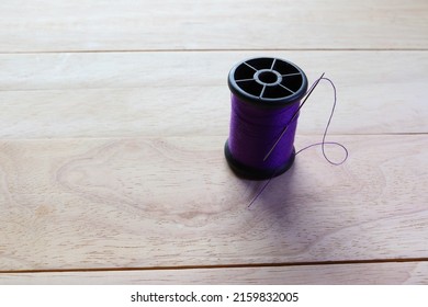 Purple thread spool and sewing needle with copy space isolated on wooden background closeup.