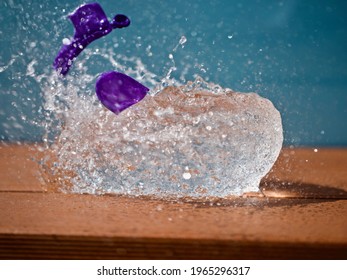 Purple Water Ballon Popping On Orange Wood Against Light Blue Background In Bright Sunlight