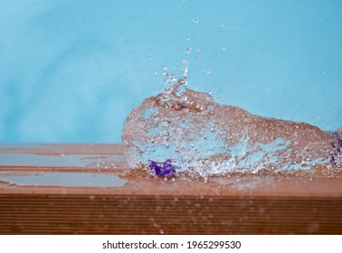 Purple Water Ballon Popping On Wet Orange Wood Against Light Blue Background