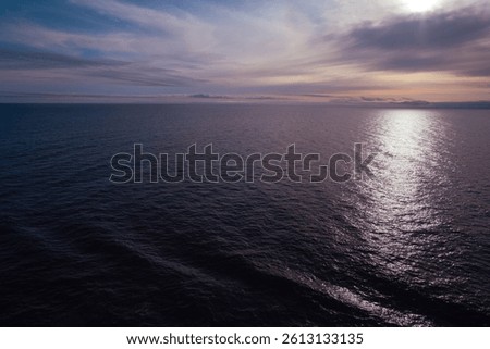 Purple whisps of clouds above calm sea at sunset