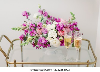 Purple And White Flower Arrangement With Champagne Glasses On Bar Cart