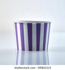 Purple and white striped takeaway disposable cardboard tub for serving food viewed low angle on grey with reflection in square format