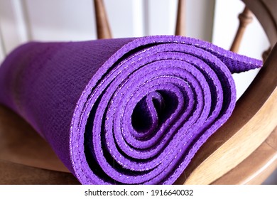 A purple yoga exercise mat rolled up on an old-fashioned vintage wooden chair in London, Ontario, Canada, February 2021.