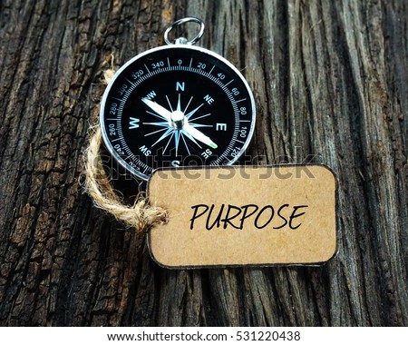 PURPOSE inscription written on paper tag, compass on old wooden background.