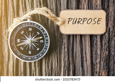 PURPOSE text written on paper tag with magnetic compass on old wooden background. A concept.