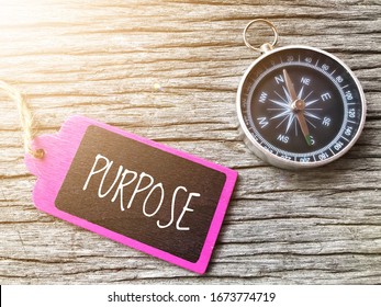 PURPOSE text written on wooden tag with magnetic compass on old wooden background. A concept.