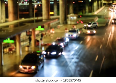 Purposely Blurred Airport Terminal Passenger Pickup Area At Night. Cars Lineup For Picking And Drop Off Travellers. Busy Road With Illuminated Headlights.