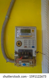 Purwokerto, Indonesia - 
December 14, 2019: Electric Meter In Indonesia On Yellow Paint Wall To 
Measure Home Prepaid Electricity Usage. Copy Space