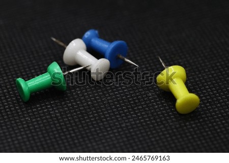 Push pins are small, thumbtack-like objects with a pointed end and a flat head, typically used to fasten items like papers or posters onto surfaces such as corkboards or walls