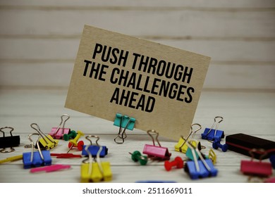 Push Through The Challenges Ahead text on paper card with stationary on wooden background