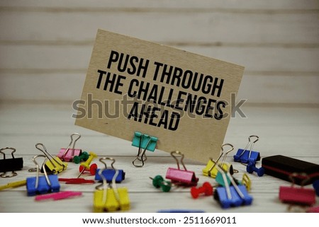 Push Through The Challenges Ahead text on paper card with stationary on wooden background