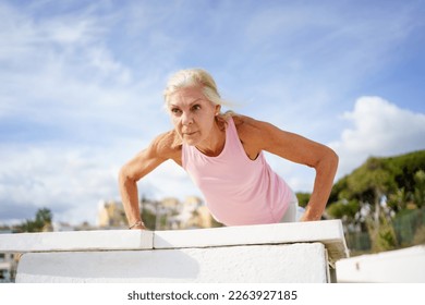 Push ups or press ups exercise by mature woman. Senior female working strength training against sky with copyspace. - Powered by Shutterstock