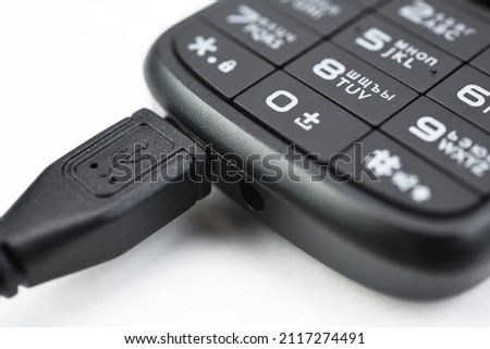Push-button mobile phone while charging. On white background. 