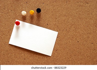A pushpin is holding a blank notecard on a cork board.
