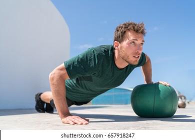 Pushup Bodybuilder Athlete Strength Training Chest And Shoulder Muscles Doing Single Arm Medicine Ball Push-ups Floor Exercises At Outdoor Gym.