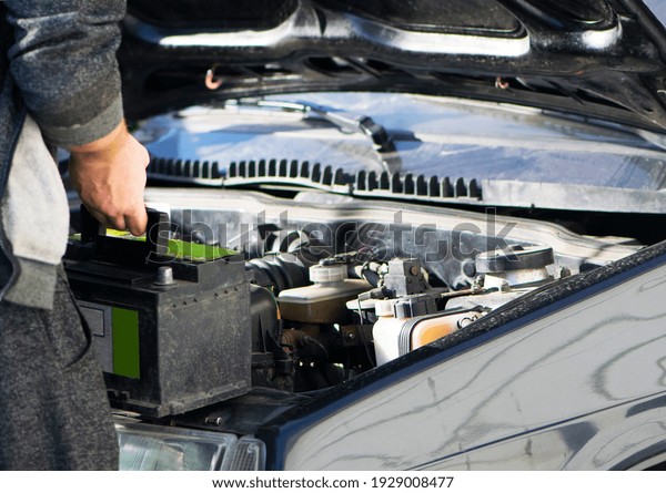 put the battery in the car, auto repair. An auto\
mechanic is about to put in the battery and tighten a new car\
battery nut in a car workshop. black car. new battery in the hands\
of the mechanic