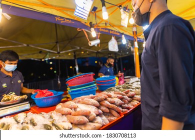 Putrajaya, Malaysia - October 09, 2020: Street food night market at  Putrajaya, near Kuala Lumpur. Salesman with face mask in a seafood street store. the customer is waiting for the fish he has bought