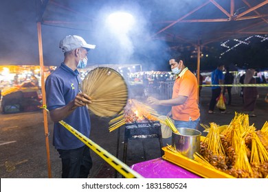 Putrajaya, Malaysia - October 09, 2020: Street food night market at  Putrajaya, near Kuala Lumpur. Two young men making satay skewers on an open fire grill. Satay is a traditional Malay dish.