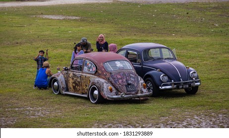 Putrajaya, Malaysia - October 11, 2020: Two Malay families meet with their old Volkswagen Beetle in a Park in Putrajaya. Two well restored VW Beetles stand on a green meadow. A girl waves friendly