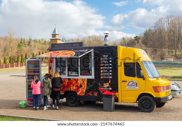 Putrishki, Belarus - April 17, 2022: People make\
an order at a pizza truck near the road. A pizzeria on wheels cooks\
pizza in an oven that is installed right in the van. The furnace\
uses real firewood