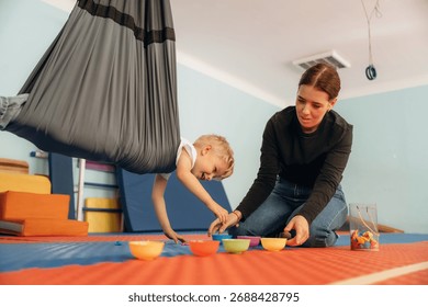 Putting the objects into bowls while hanging. Preschool child with teacher during developmental activities in a playroom.