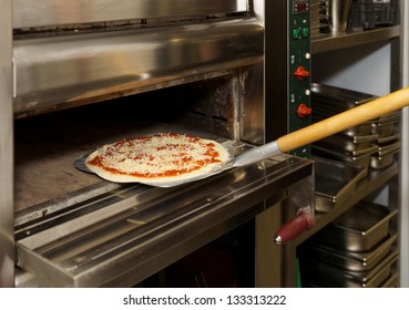 Putting Pizza In Oven At Restaurant Kitchen