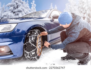 Putting winter chains on car. Man's hands putting on snow chains on the car wheel on the icy road at winter mountains.