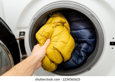 Putting winter jacket into the drum of open washing machine in laundry room. Washing dirty down jacket in the washer