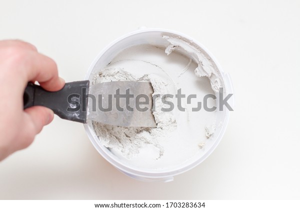 putty knife on worker hand and tub of white\
acrylic glazing putty.