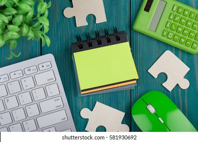 Puzzle pieces, calculator, sketchbook, computer keyboard and mouse on a blue wooden background