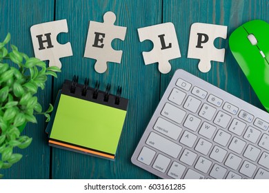 Puzzle pieces with word "help", note pad, computer keyboard and mouse on a blue wooden background