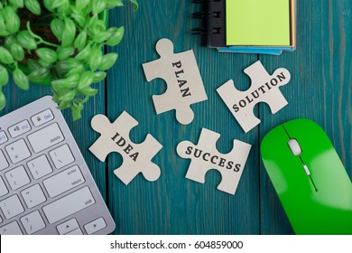 Puzzle pieces with words "idea", "plan", "solution", "success", sketchbook, computer keyboard and mouse on a blue wooden background
