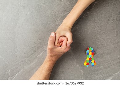 Puzzle Ribbon With Hands Clasped Together On Gray Background, Mental Health Care Concept. Concept Of Helping Those In Need World Autism Awareness Day