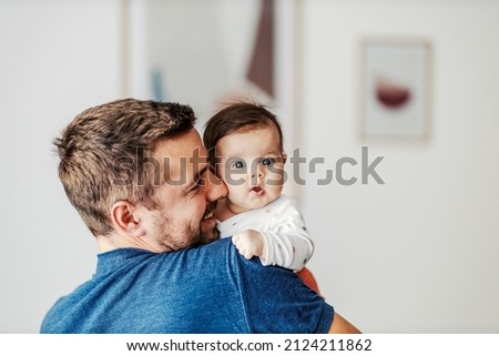 A puzzled baby girl in father's arms looking at the camera.
