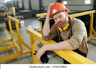 Puzzled Bearded Factory Worker Keeping Eyes Closed And Leaning On Yellow Metal Railing While Thinking Of Production Problems At Factory