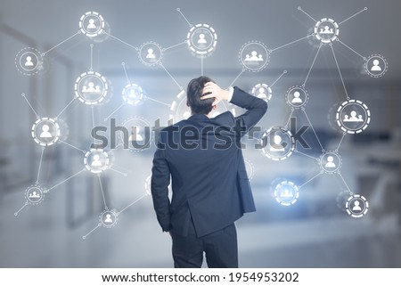 Puzzled businessman looking at the multiple application hologram icons with coworking space in the background, social media and communication concept
