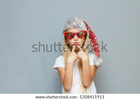 Puzzled Christmas girl in Santa hat and sunglasses stylized sixties on grey background