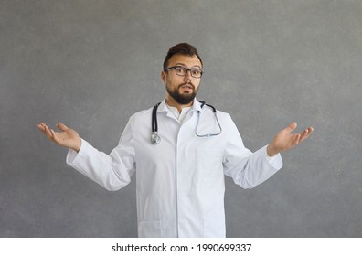 Puzzled Clueless Adult Male Doctor With Arms Out, Shrugging Shoulders Saying Who Cares, So What, Dont Know. Emotions, Facial Expressions, Life Perception And Attitude. Studio Shot Over Grey Background