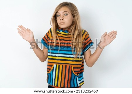 Puzzled and clueless beautiful caucasian teen girl wearing striped sweater over white studio wall  with arms out, shrugging shoulders, saying: who cares, so what, I don't know. [[stock_photo]] © 