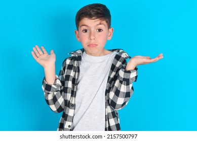 Puzzled And Clueless Caucasian Kid Boy Wearing Plaid Shirt Over Blue Background With Arms Out, Shrugging Shoulders, Saying: Who Cares, So What, I Don't Know.