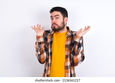 Puzzled And Clueless Young Caucasian Man Wearing Plaid Shirt Over White Background With Arms Out, Shrugging Shoulders, Saying: Who Cares, So What, I Don't Know.