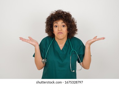 Puzzled and clueless young doctor woman with arms out, shrugging her shoulders, saying: who cares, so what, I don't know. Negative human emotions, facial expressions, life perception and attitude