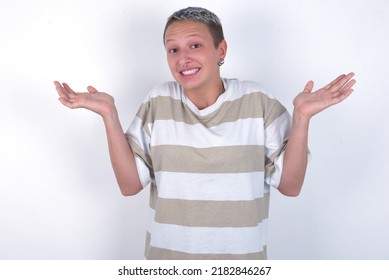 Puzzled and clueless young woman with short hair wearing striped t-shirt over white background with arms out, shrugging shoulders, saying: who cares, so what, I don't know. - Powered by Shutterstock