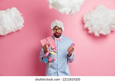 Puzzled Confused Bearded Adult Man Holds Toy And Baby Bottle Poses With Nipple In Mouth Feels Confused Has No Experience Of Caring About Baby Wears Diaper On Head Shirt And Bowtie Poses Indoors