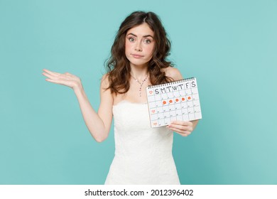 Puzzled confused bride woman in white wedding dress hold female periods calendar checking menstruation days spreading hands isolated on blue turquoise background. Ceremony celebration party concept