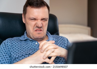 Puzzled And Confused Man Who Looks At Laptop Screen At Workplace In Hotel Office. Confused Millennial Man Reading News On Laptop With Disgust, Unpleasant Negative Emotions. 