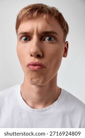 Puzzled expression on a closeup of a young man, wide eyes and pursed lips, capturing surprise, confusion, and curiosity in a simple studio setting for expressive stock imagery